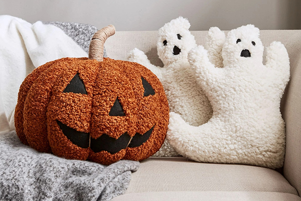 A mix of square and novelty-shaped Halloween pillows, like a ghost and a pumpkin